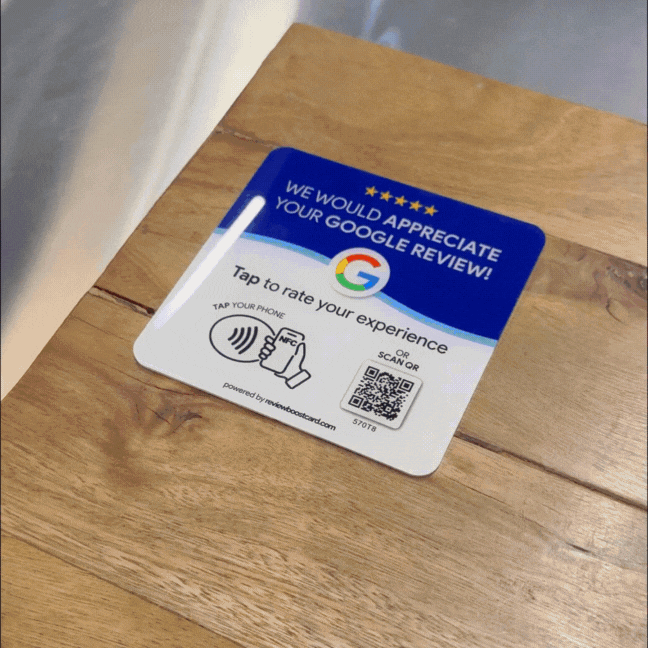 GIF showing a Google review plaque on a wooden surface being used. The plaque features Google logo with text 'We would appreciate your Google review!' and NFC tapping symbol, along with a QR code for easy scanning